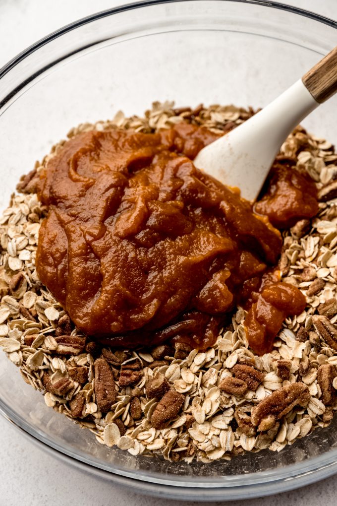 A bowl of pumpkin granola ingredients getting stirred together with a spatula.