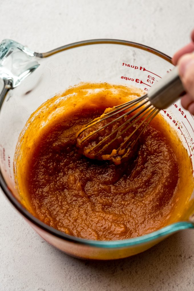 The wet ingredient portion of pumpkin granola being stirred with a whisk in a large glass measuring cup.