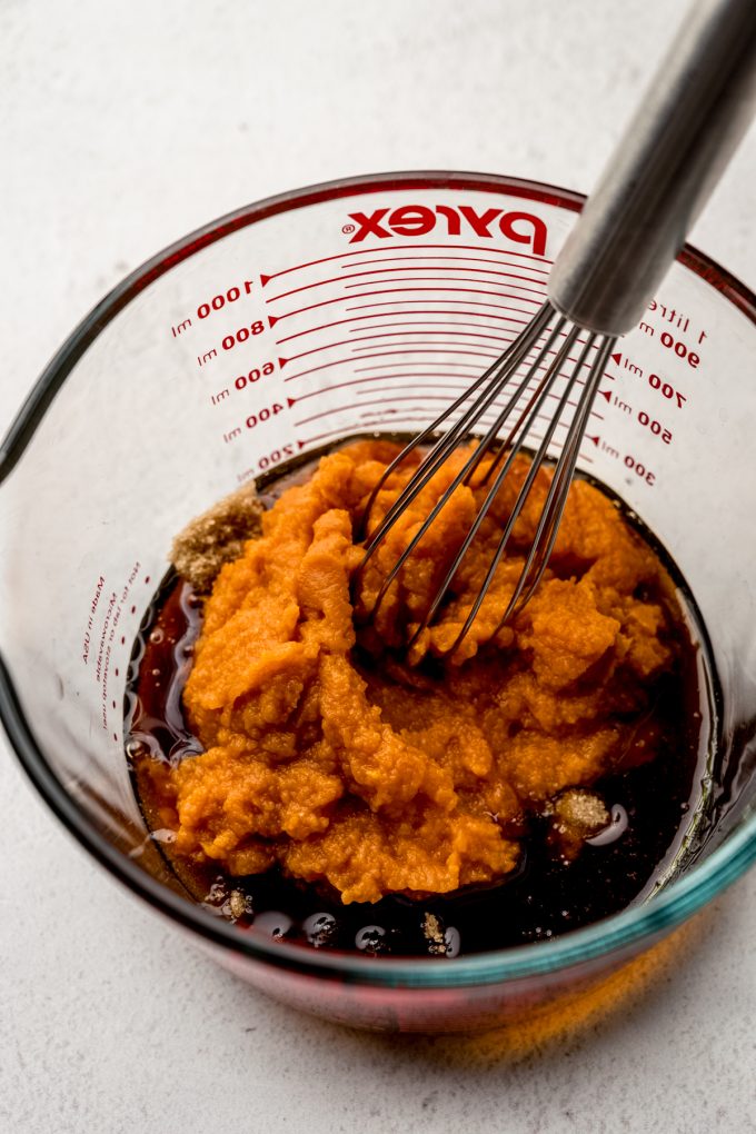 A large measuring cup with pumpkin and other ingredients in it getting stirred with a whisk.