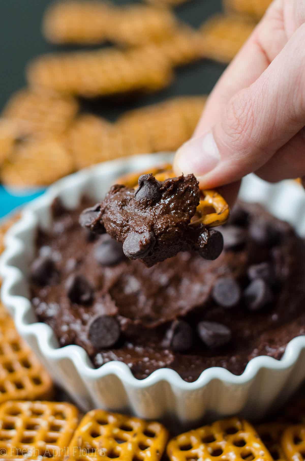 hand dipping a pretzel into brownie batter dip
