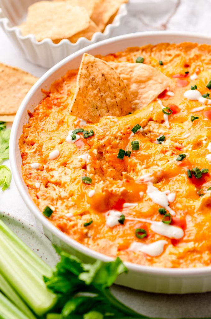 A dish of buffalo chicken dip with chips dipped into it.