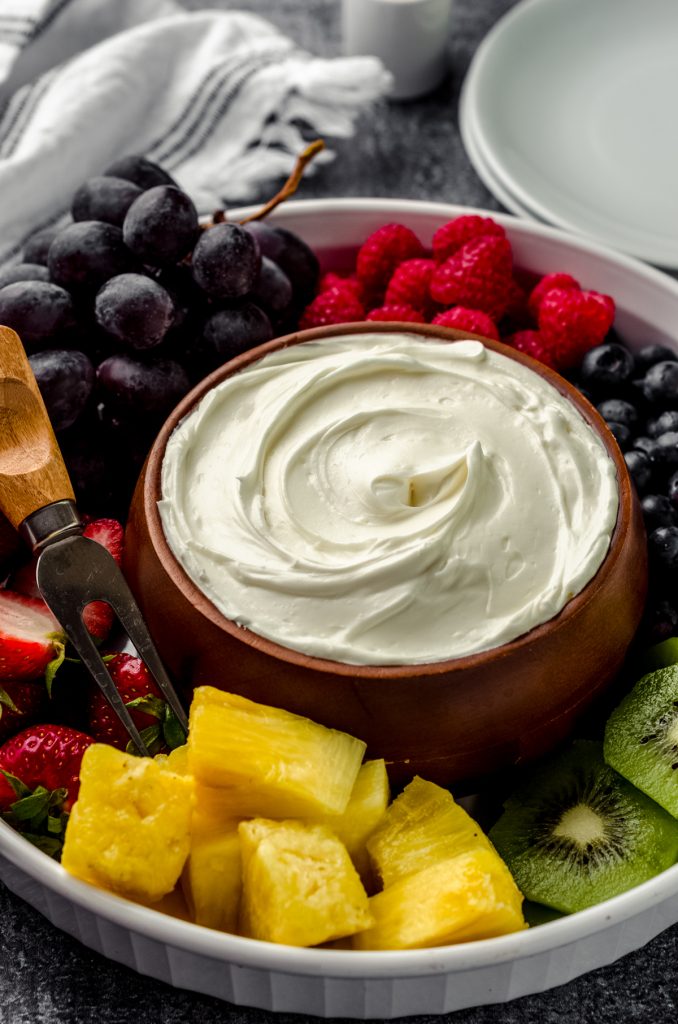 A bowl of fruit dip surrounded by a variety of sliced fruits.