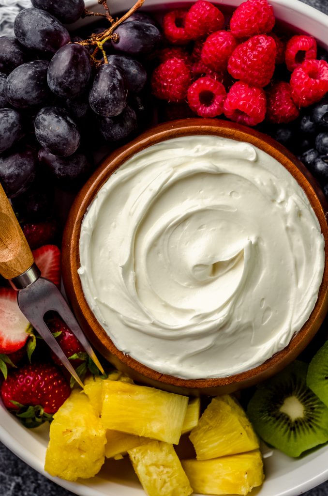 A bowl of fruit dip surrounded by a variety of sliced fruits.