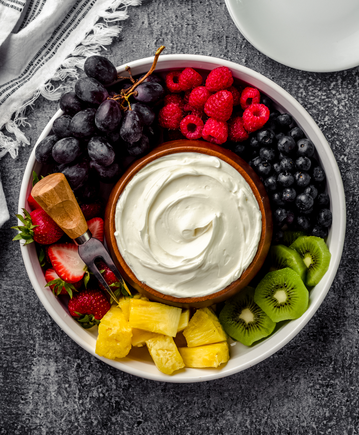Aerial photo of a bowl of fruit dip surrounded by a variety of sliced fruits.