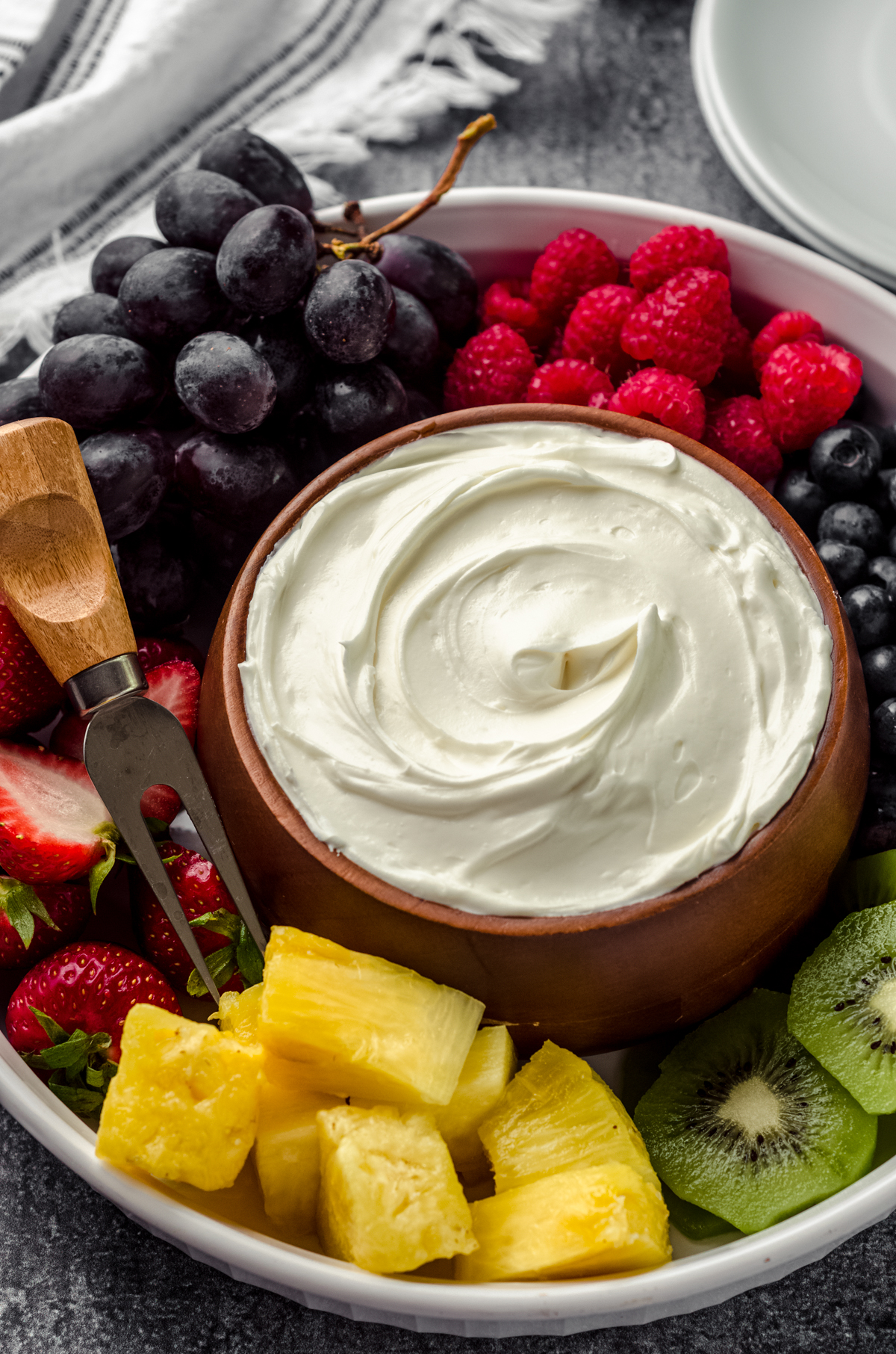 A bowl of fruit dip surrounded by a variety of sliced fruits.