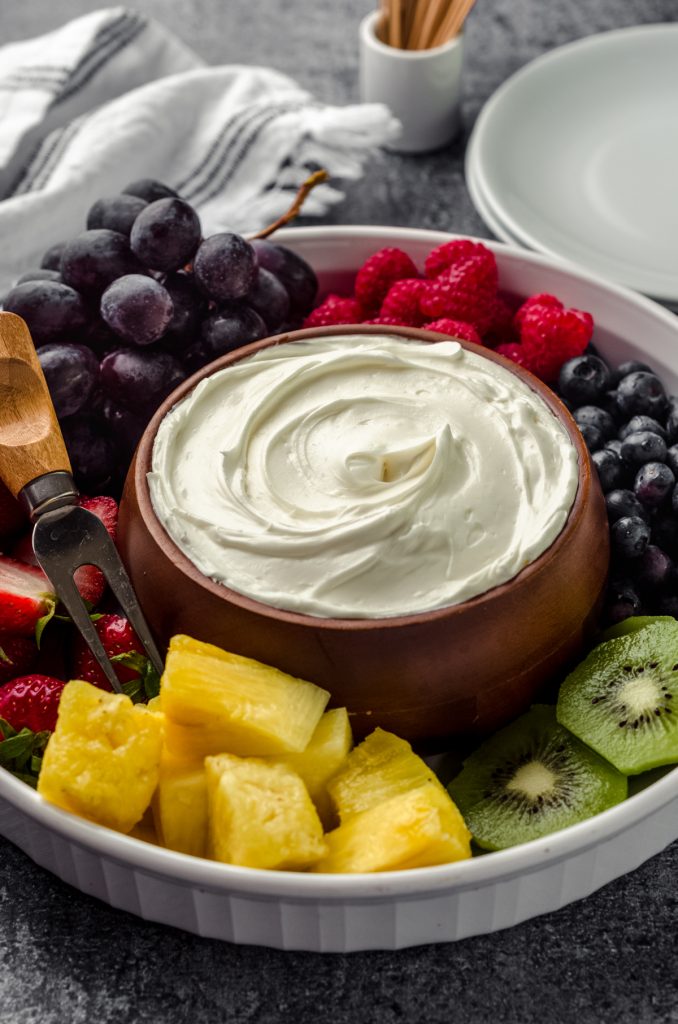 A bowl of fruit dip surrounded by a variety of sliced fruits.