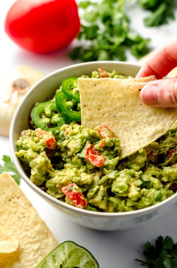Someone is dipping a tortilla chip into a bowl of fresh guacamole.