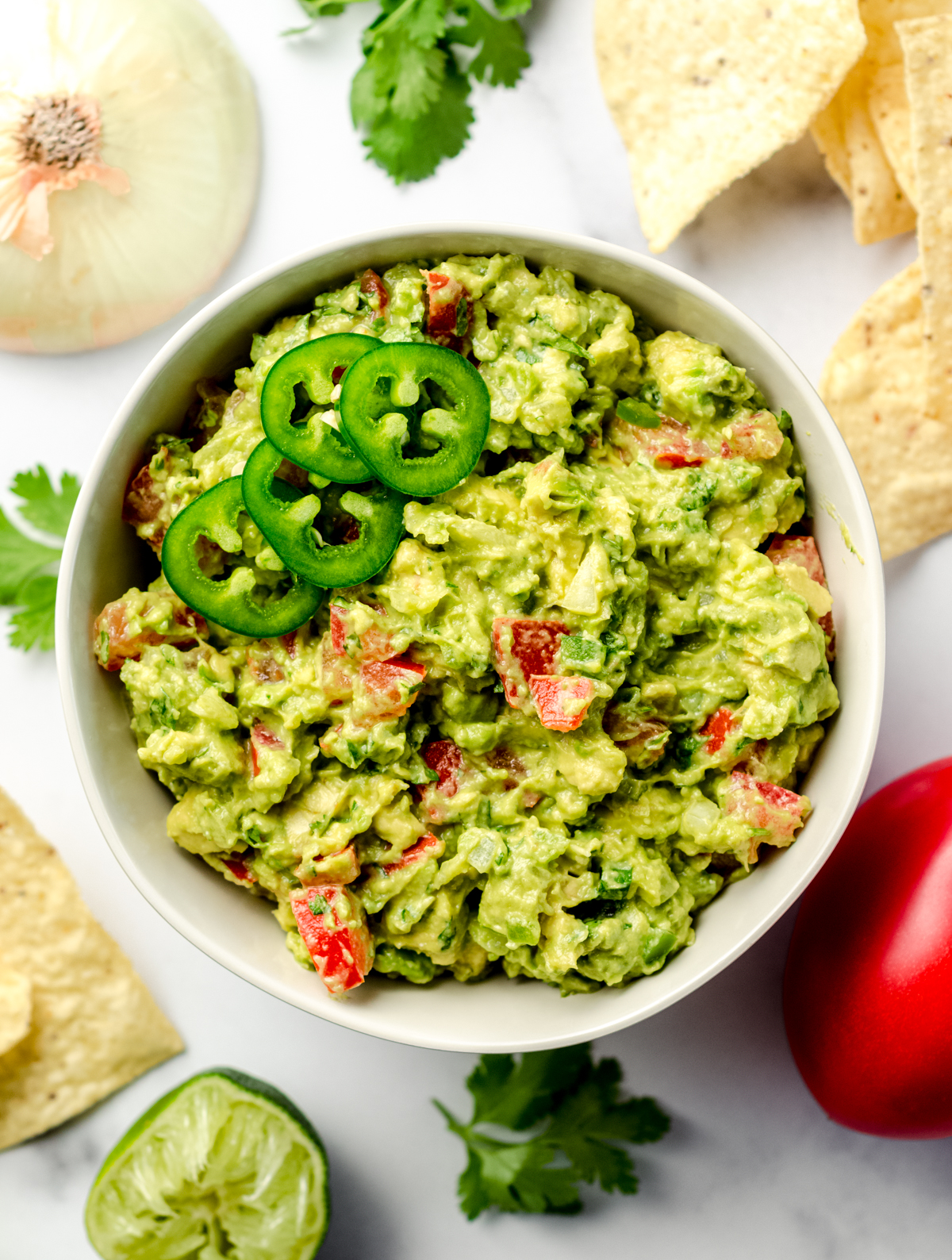 Aerial photo of homemade guacamole in a bowl with ingredients and chips scattered around it.