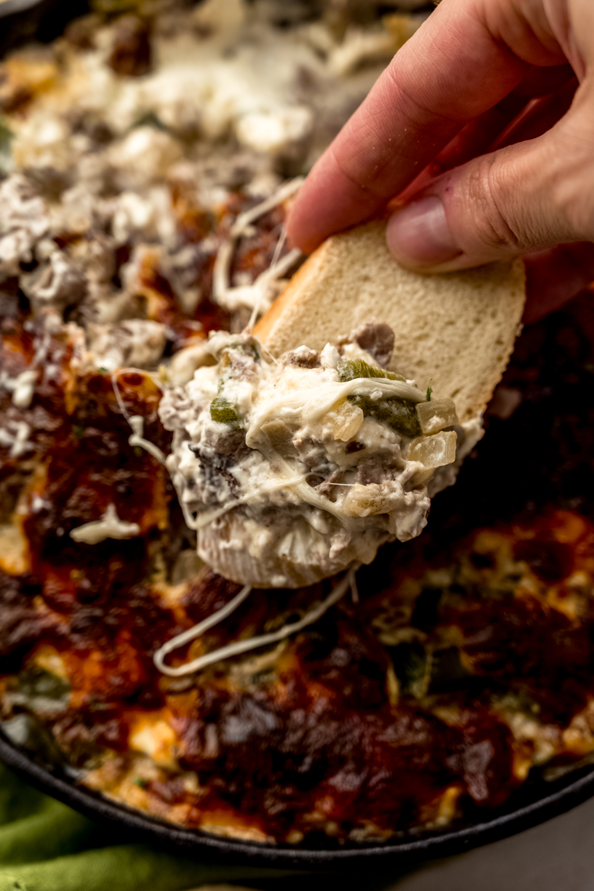 Someone holding a baguette piece that has been dipped into Philly cheesesteak dip.