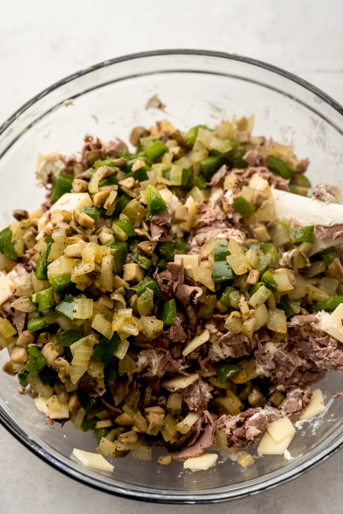 A glass bowl of the ingredients to make Philly cheesesteak dip.