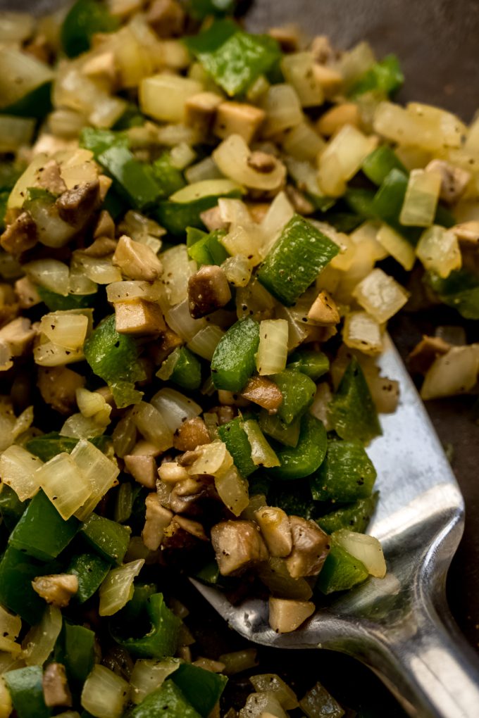 Onions, peppers, and mushrooms that have been cooked in a pan with a spatula.