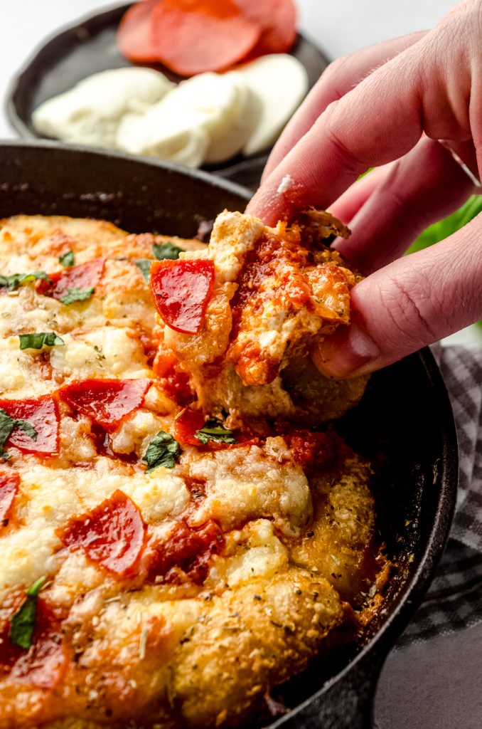 Someone is grabbing a roll from a ring of pizza dip in a skillet.