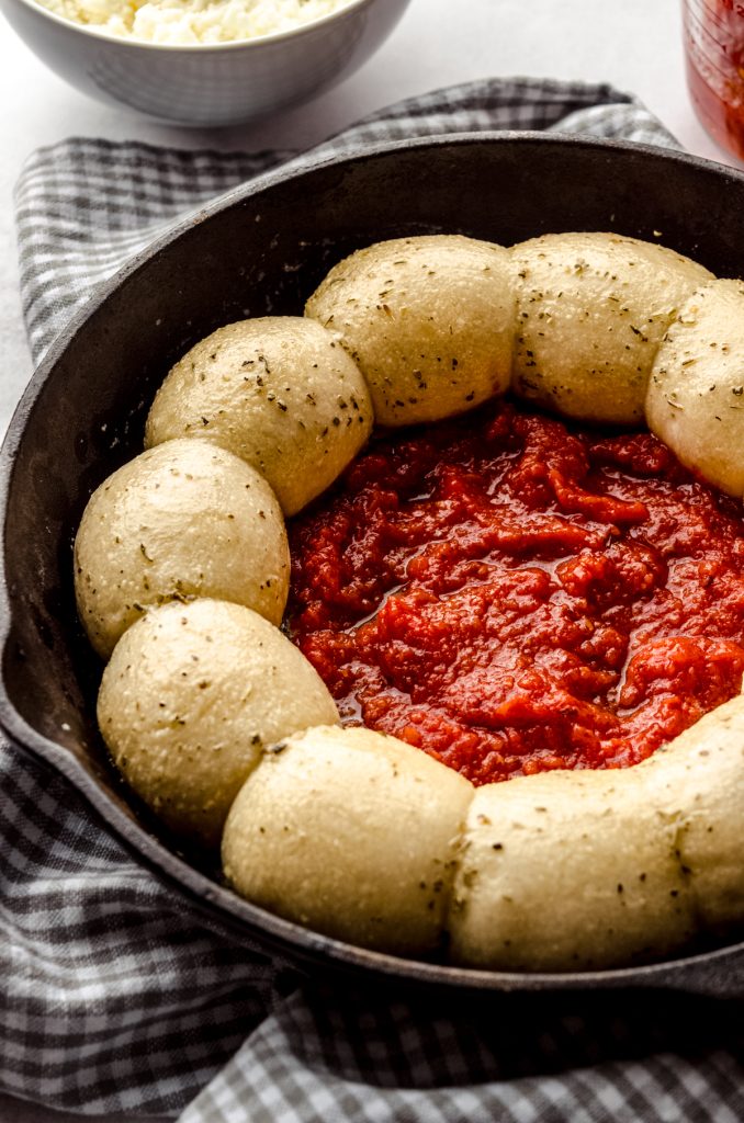 Dinner rolls in a ring in a skillet with a puddle of pizza sauce in the middle ready to bake pizza dip.