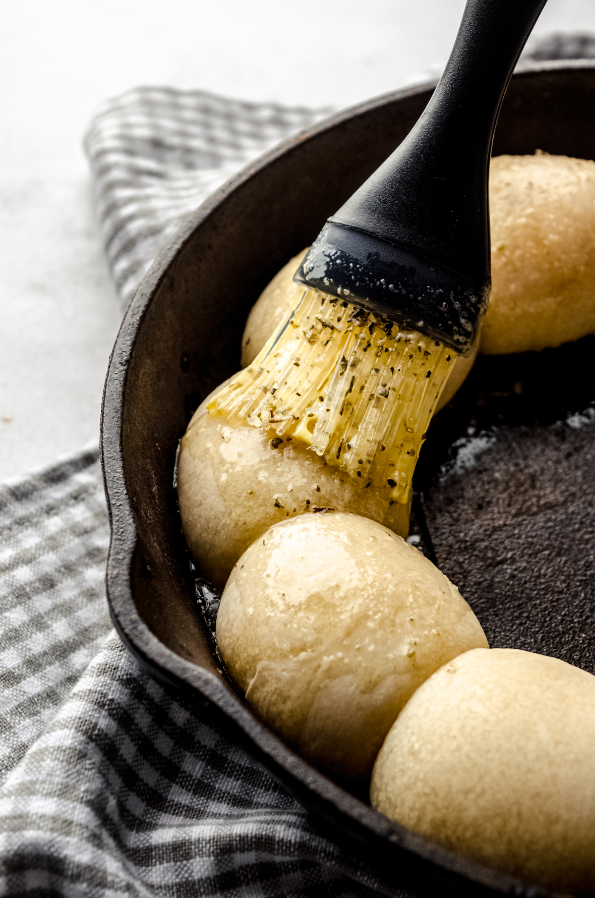 Someone is using a pastry brush to brush seasoned butter onto rolls in a skillet.