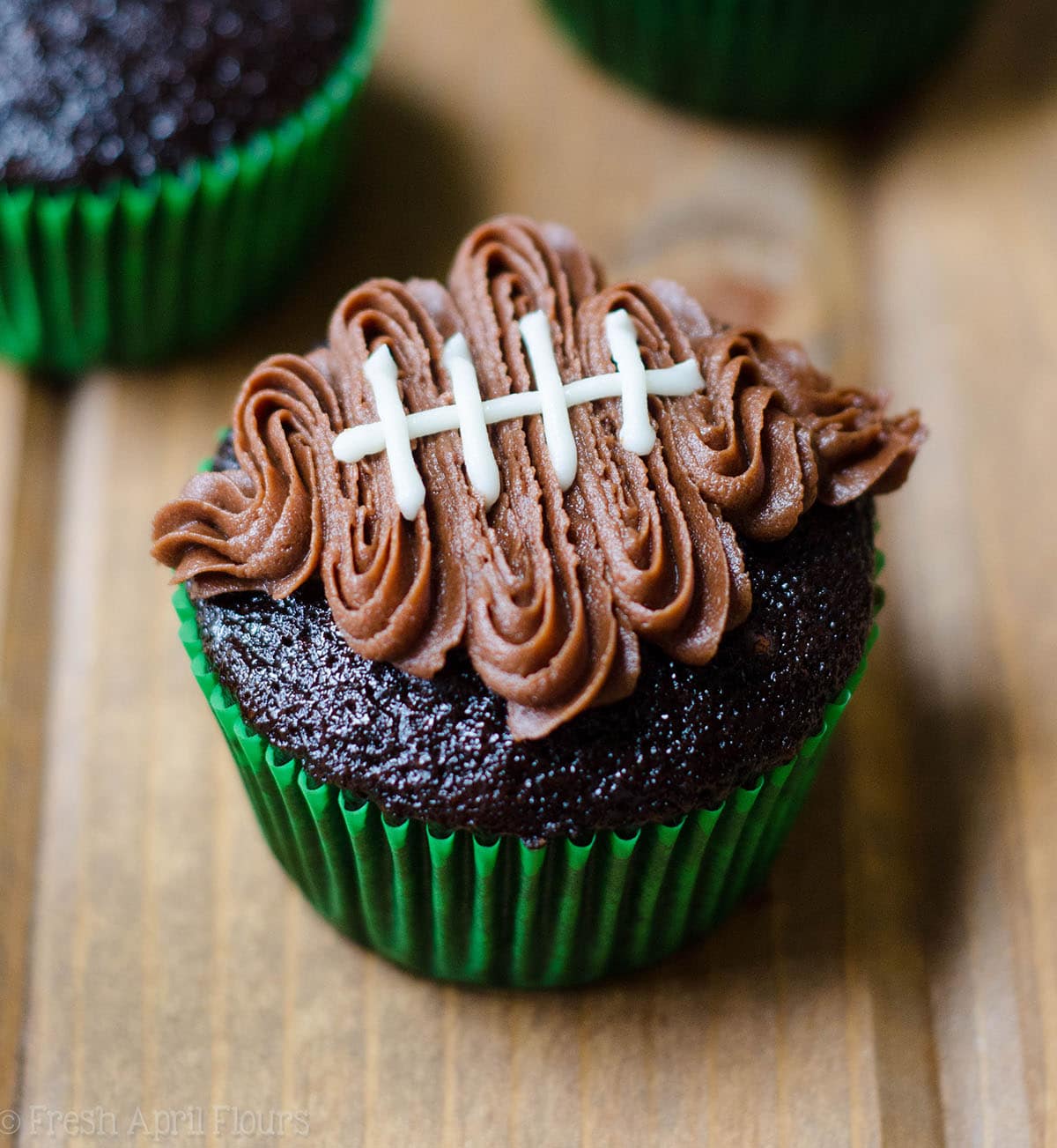 chocolate cupcake in a green cupcake liner with a chocolate frosting football piped on top to make football cupcakes