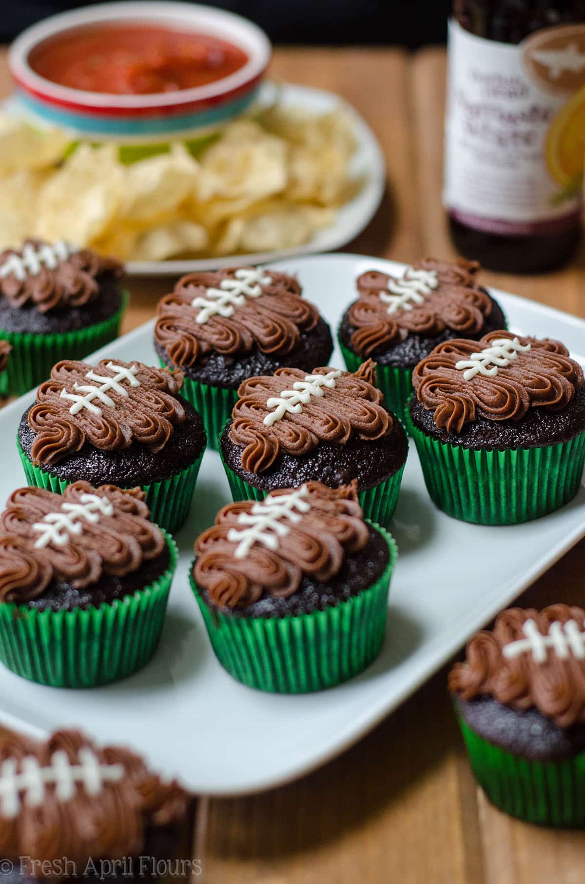 chocolate cupcakes in green cupcake liners with a chocolate frosting footballs piped on top to make football cupcakes