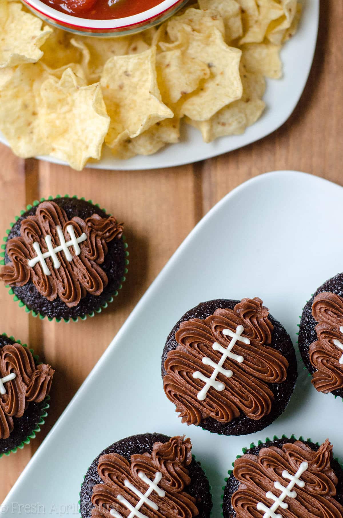 aerial photo of chocolate cupcakes in green cupcake liners with a chocolate frosting footballs piped on top to make football cupcakes