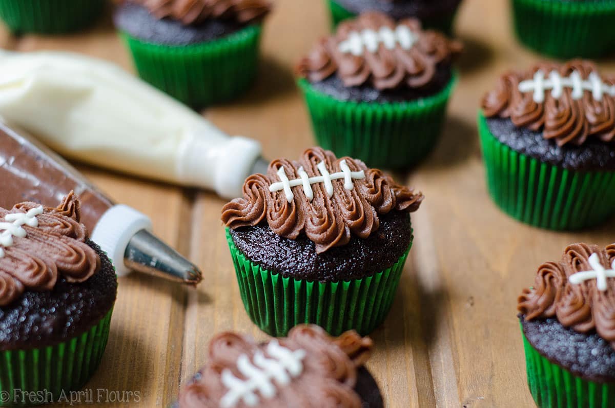 chocolate cupcakes in green cupcake liners with a chocolate frosting footballs piped on top to make football cupcakes