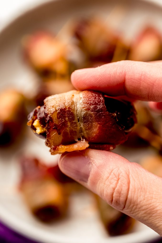 Someone is holding a bacon wrapped date with goat cheese.