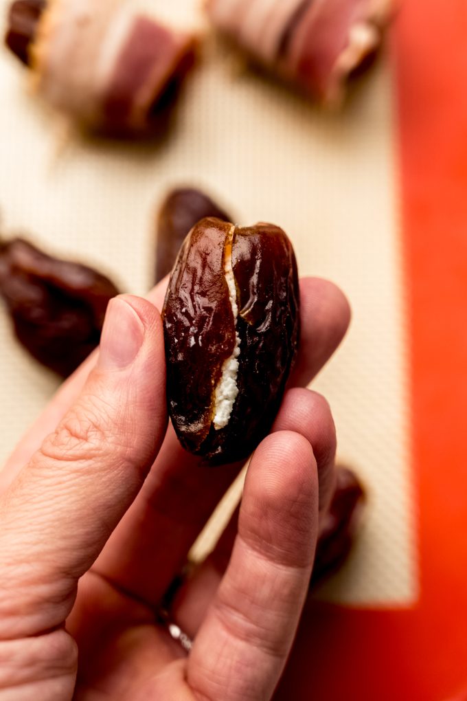 Someone is holding a date that has been split open and stuffed with goat cheese.