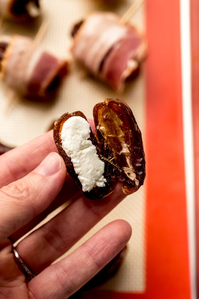 Someone is holding a date that has been split open and stuffed with goat cheese.