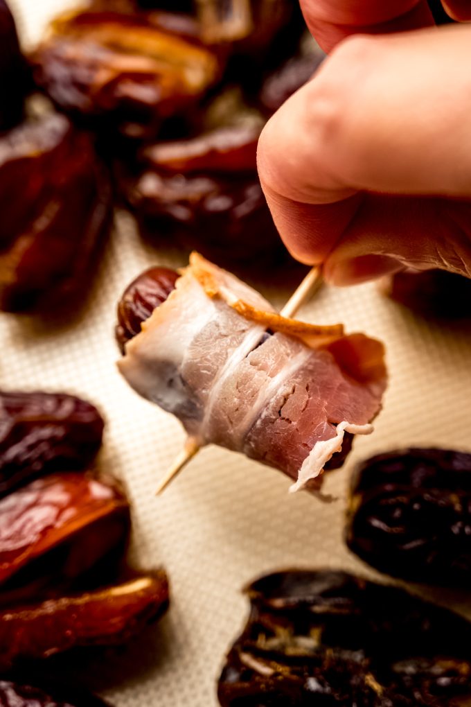 Someone holding a bacon wrapped date with the toothpick.