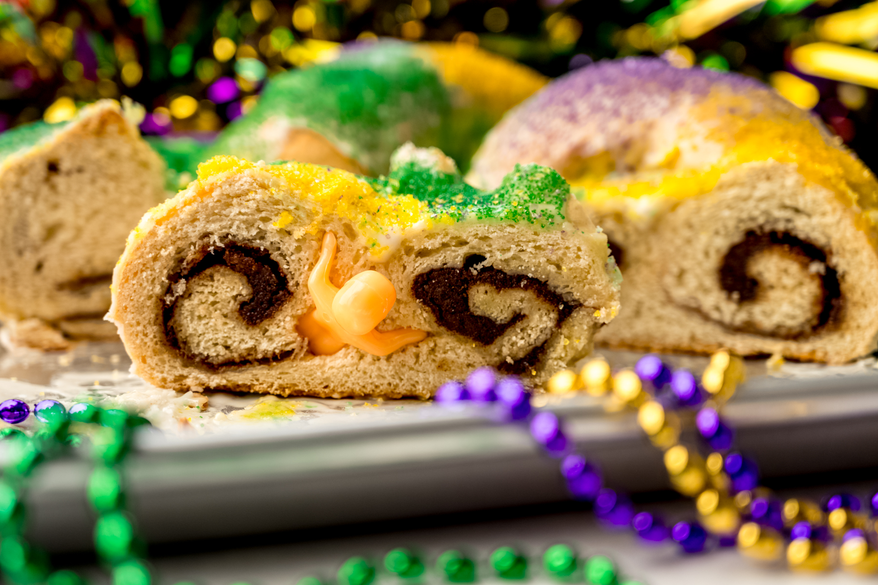 A slice of Mardi Gras king cake on a platter with beads and decor around it.