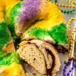 A Mardi Gras king cake that has been sliced and sitting on a surface and one slice is on its side so you can see the inside of it.
