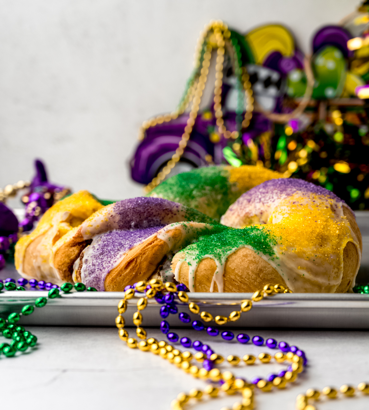 A Mardi Gras king cake on a platter with decor and beads all around it.