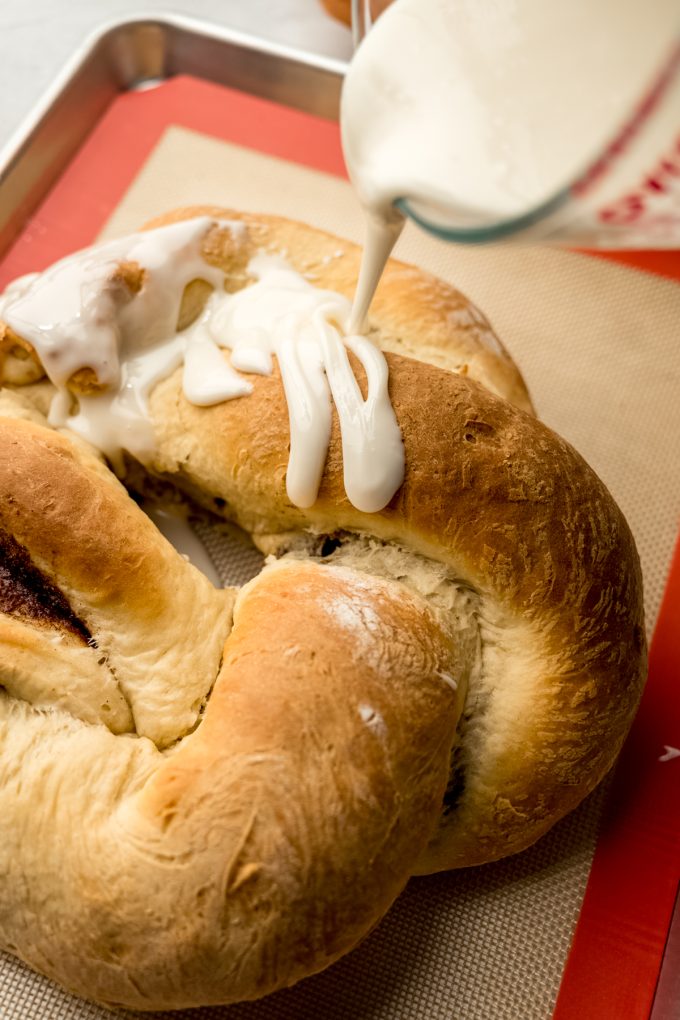 Someone is pouring icing onto a Mardi Gras king cake.