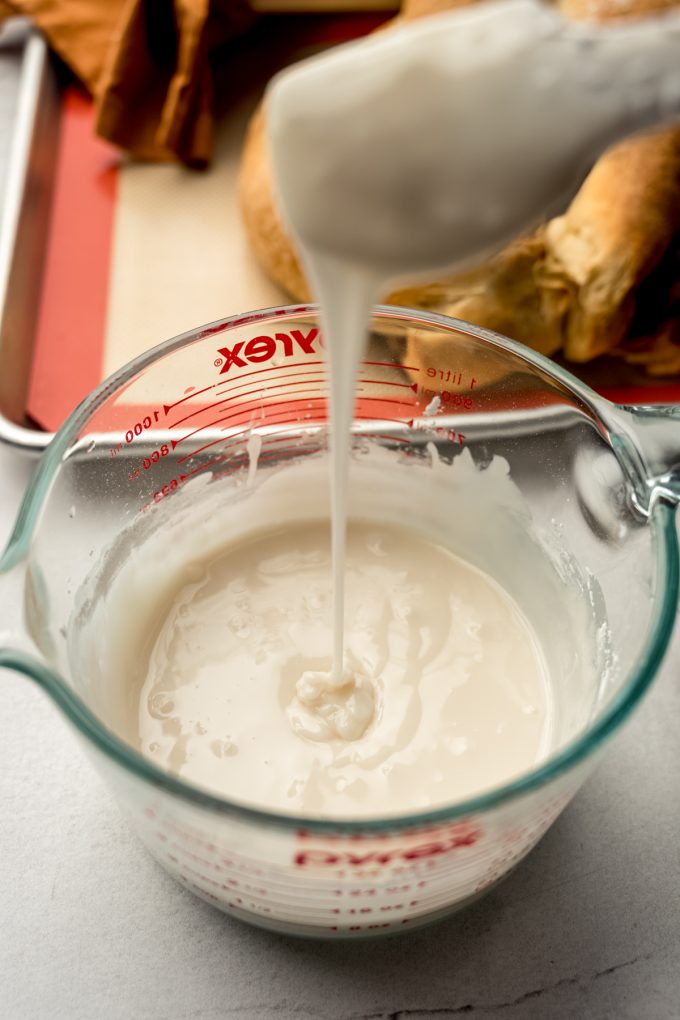 Someone is holding a spatula over a bowl of icing and letting it drip back into the bowl.