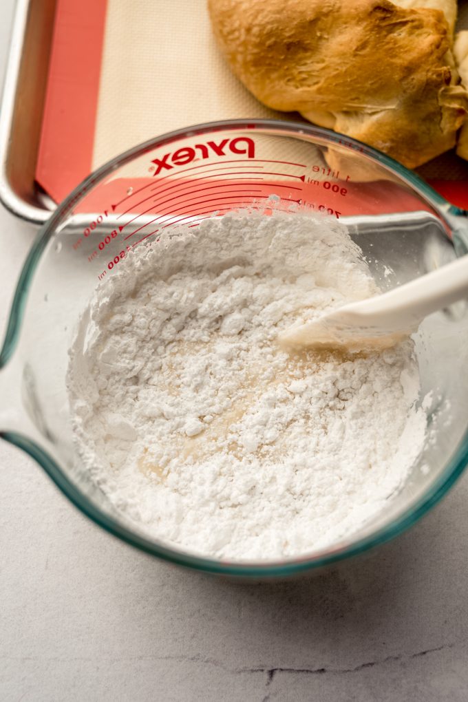 Someone is stirring icing with a spatula in a glass measuring cup.
