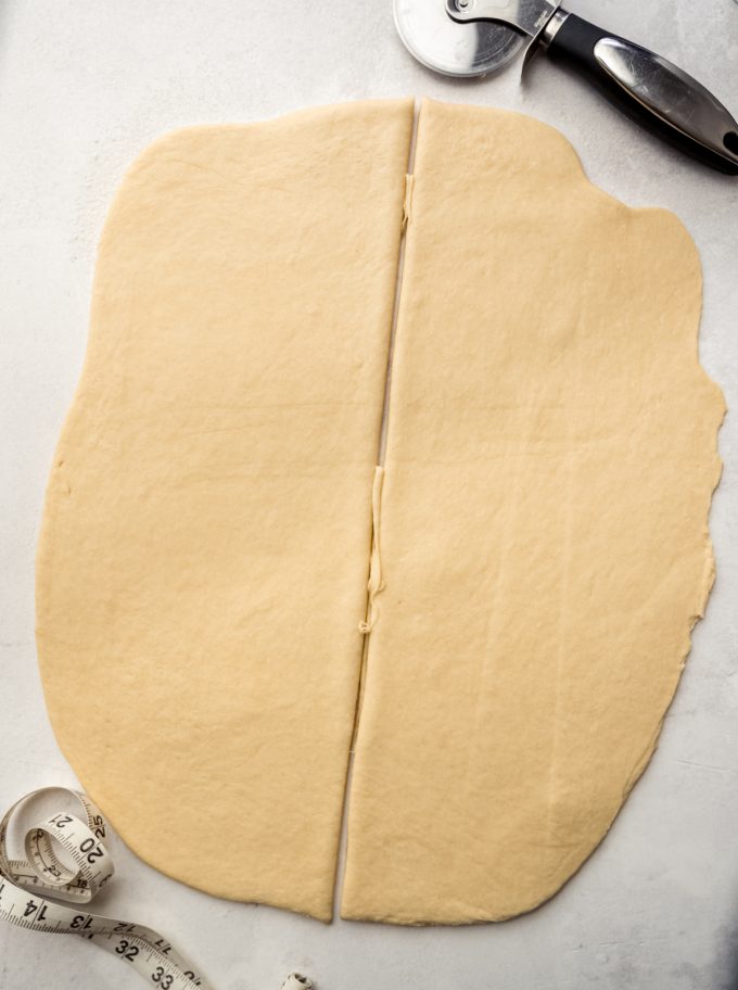 A rectangle of dough to make Mardi Gras king cake that has been cut in half.