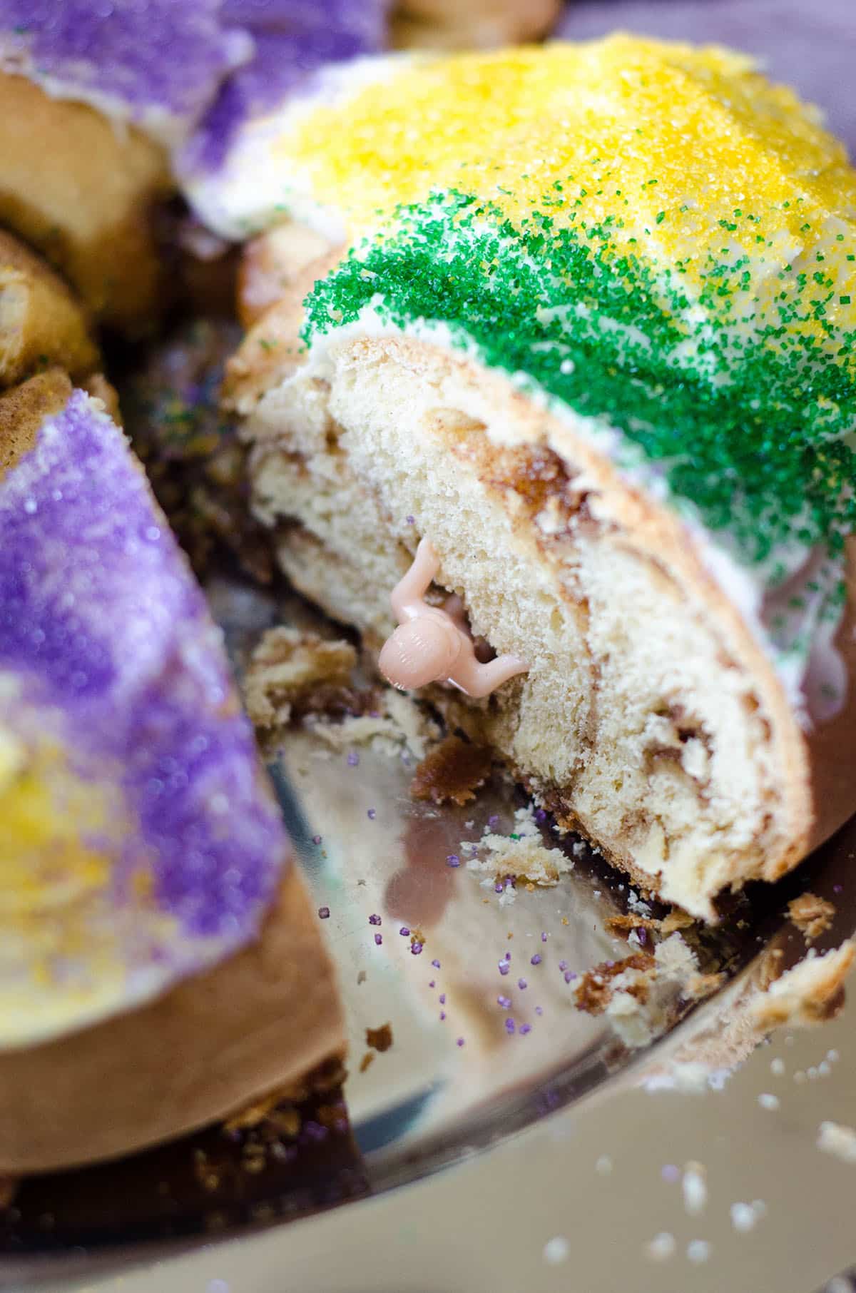 sliced mardi gras cake with a baby sticking out of it