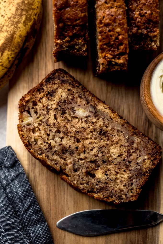 Aerial photo of a slice of banana nut bread on a cutting board.