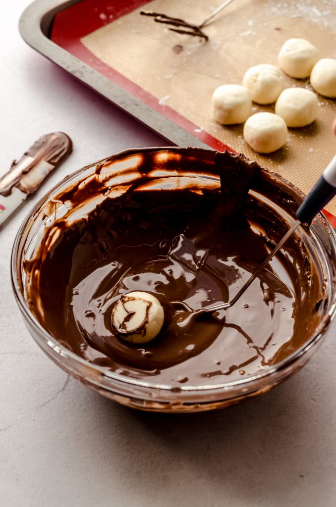 Someone is dipping a buttercream round into chocolate coating to make Easter candy.