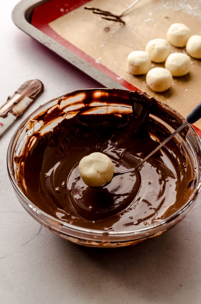 Someone is dipping a buttercream round into chocolate coating to make Easter candy.