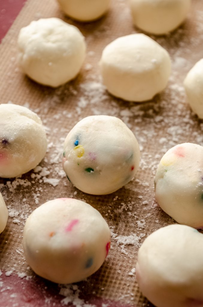 Funfetti buttercream rounds filling on a baking sheet before getting dipped in chocolate.