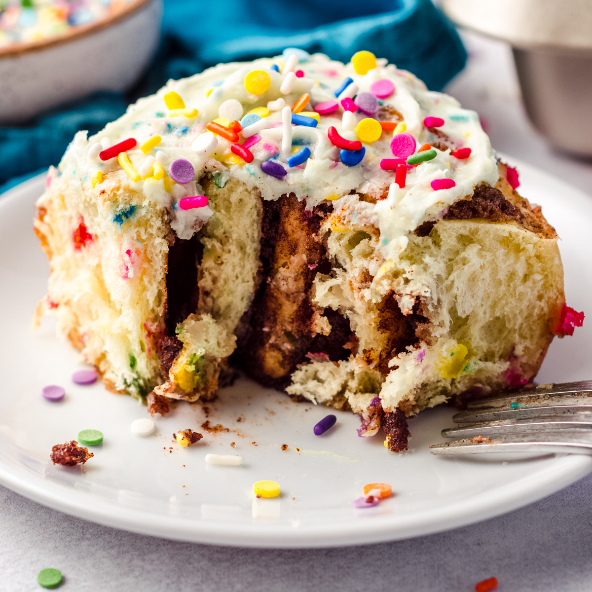 A funfetti cinnamon roll on a plate with a bite taken out of the roll.