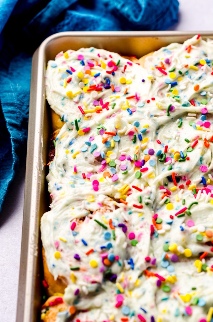 Funfetti cinnamon rolls in a baking pan with rainbow chip frosting on top.