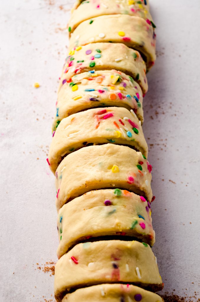 Sliced funfetti cinnamon rolls on a surface before getting placed into a baking pan.