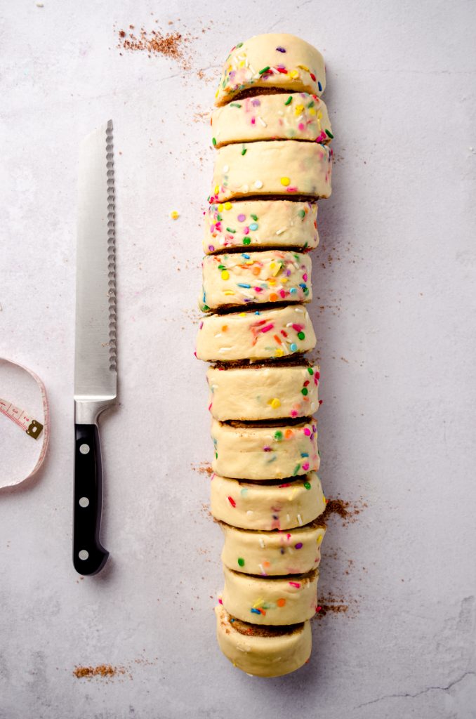 Aerial photo of sliced funfetti cinnamon rolls with a knife and measuring tape around them.