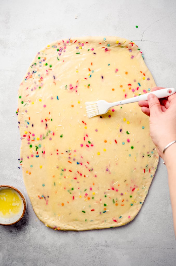 Aerial photo of someone brushing butter onto funfetti cinnamon roll dough.