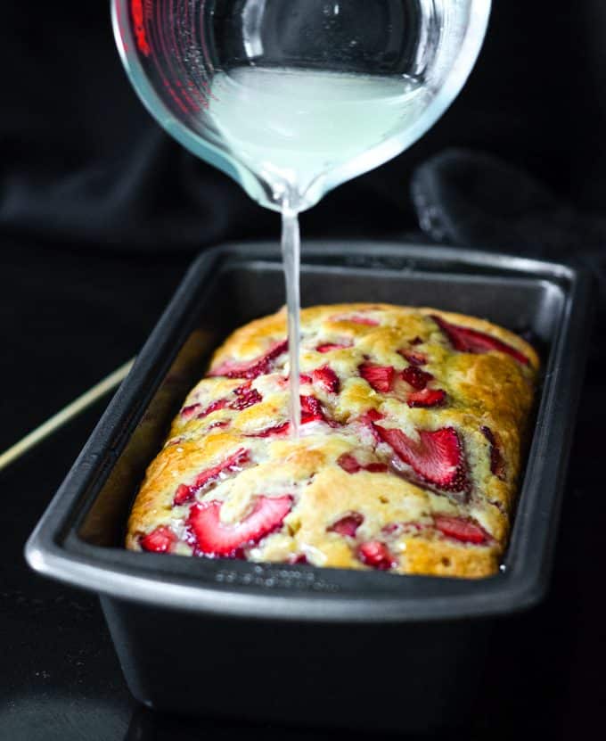 pouring lemon syrup onto strawberry lemonade quick bread 