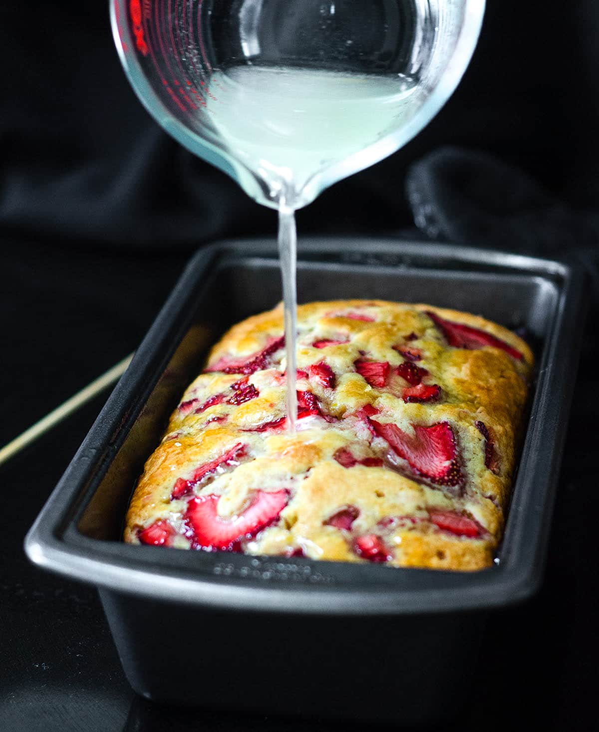 pouring lemon syrup onto strawberry lemonade quick bread 