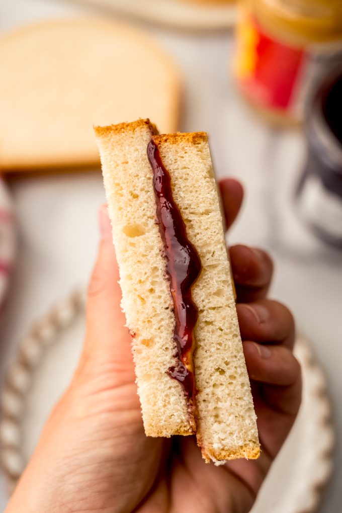 Someone's hand holding half of a peanut butter and jelly sandwich.