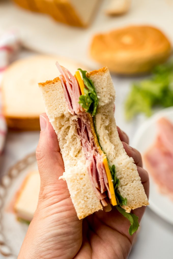 Someone's hand holding a ham and cheese sandwich with a bite taken out of it.