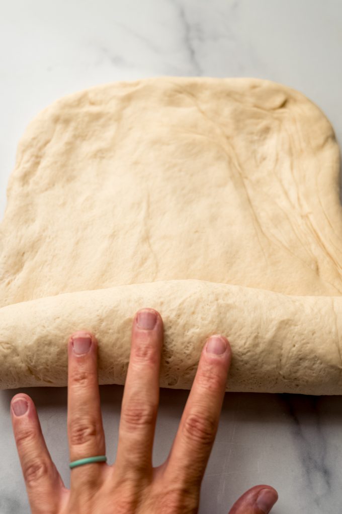 Someone is using their hand to roll up sandwich bread dough into a log.