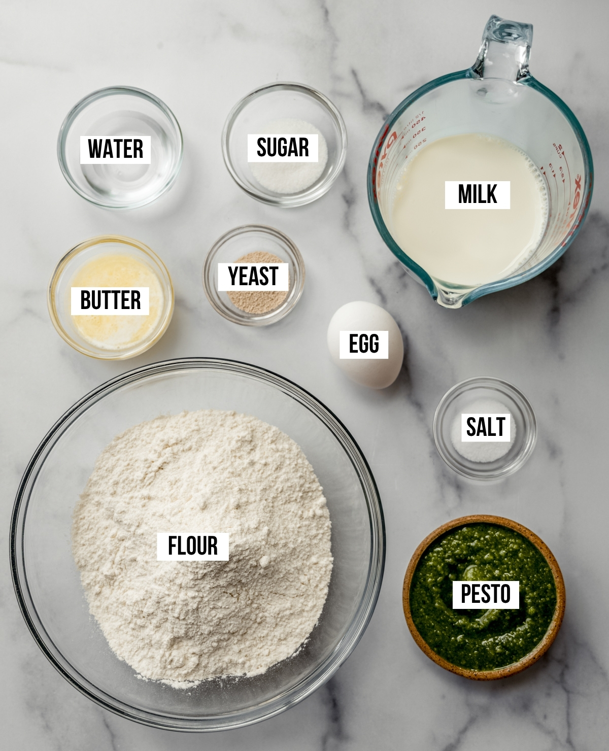 Aerial photo of ingredients to make pesto pull-apart bread with text overlay labeling each ingredient.