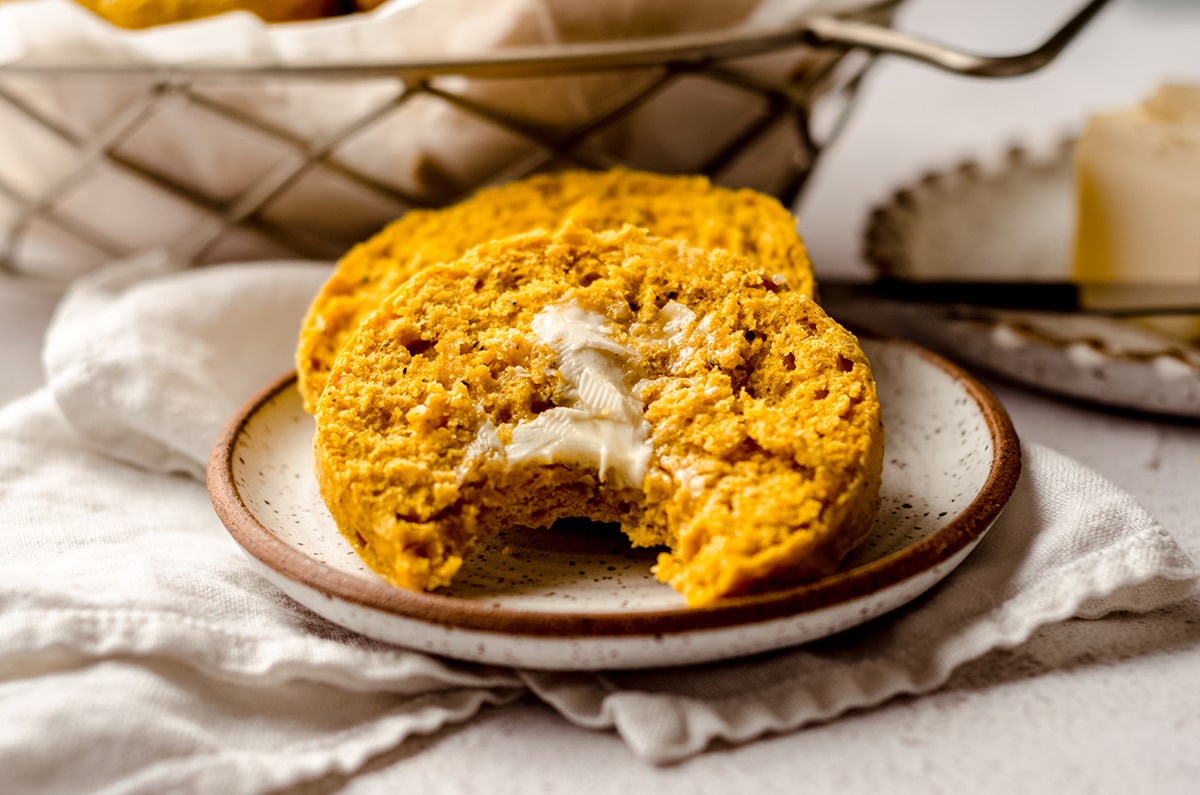 buttered pumpkin biscuits on a plate and one has a bite taken out of it